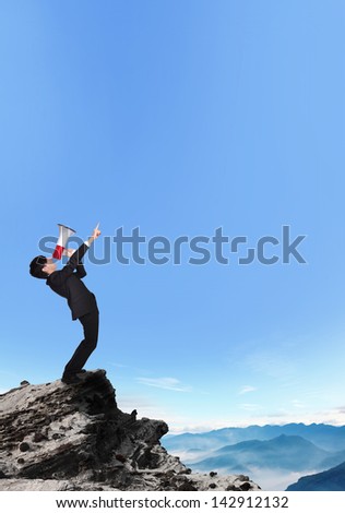 business man shouting into a megaphone and finger point to copy space on a mountain, asian model