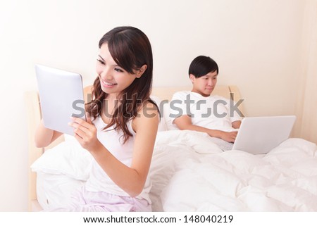 Cheerful couple using touch pad and computer in bed at home, asian people