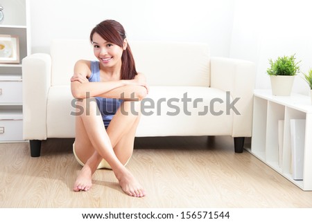 Smiling young woman sitting on floor with her couch at home, asian beauty