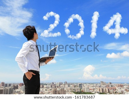 Young Business Man Using Laptop And Look To 2014 Year Text With Blue Sky And Cloud And Cityscape In The Background, Business And Cloud Computing Concept