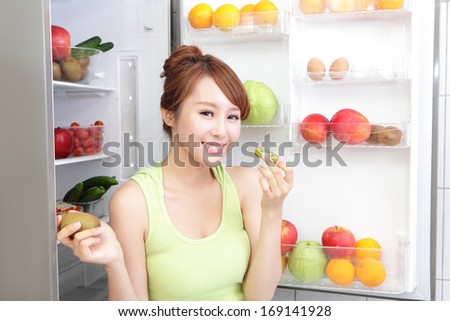 Healthy Eating Concept .Diet. Beautiful Young Woman eat kiwi fruit near the Refrigerator with healthy food. Fruits and Vegetables, asian model