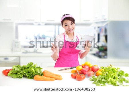 Young woman wearing kitchen apron with digital tablet in kitchen with fresh produce vegetables preparing for a healthy meal, asian