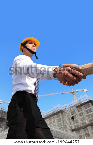 Worker and architect shaking hands at construction site comparing housing project with building, focus on hand