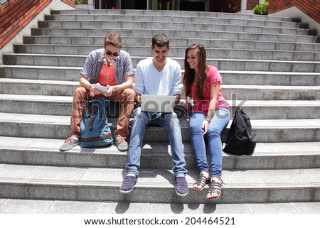 Happy students sitting on stairs using digital tablet and conservation to each other in school, caucasian