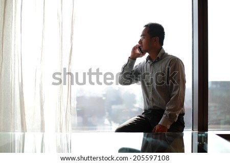 Young business man talking on phone with window in hotel, asian