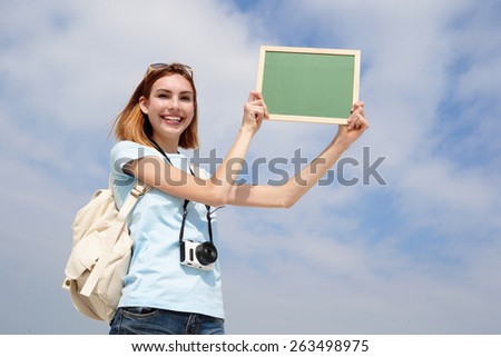 Happy travel woman smile to you and show empty chalkboard with sky background, caucasian beauty