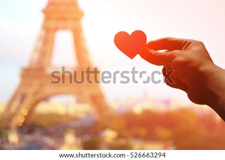 silhouette of romantic lovers hand hold love heart paper with eiffel tower in Paris with sunset