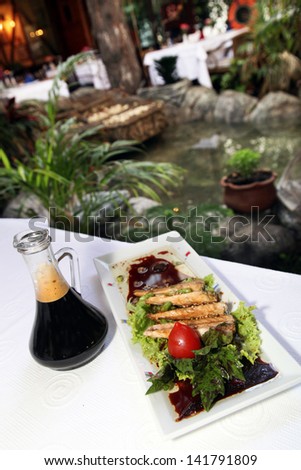 Turkish sea food \'Pike perch fillet\' and soy sauce bottle with vegetables on the dinner plate.