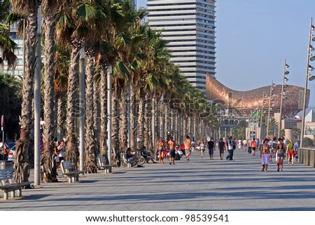 BARCELONA, SPAIN - AUGUST 14: People walking on Barceloneta Palm road, August 14, 2009 in Barcelona, Spain. Frank Gehry\'s Peix d\'Or (Whale Sculpture) is seen at the end of the road.
