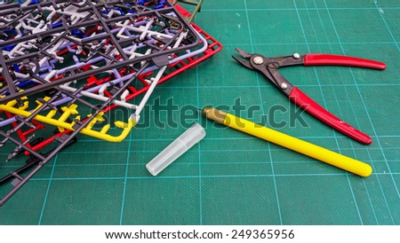 An art knife and a clipper for plastic model with stack of plastic part frames on a green cutting board