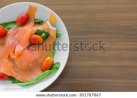Rocket salad with smoked salmon and cherry tomatoes in a white dish on a wooden table