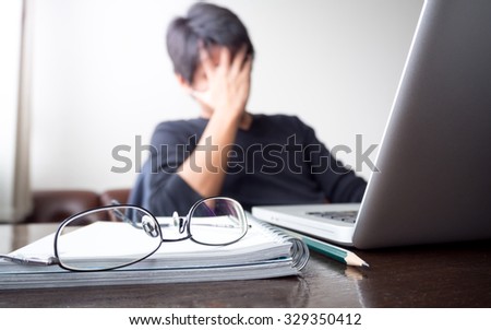 man with his hand holding his face taking a brake from working with laptop computer and notebook with eye glasses on wooden desk. concept of stress/rest/tension/failed/discourage
