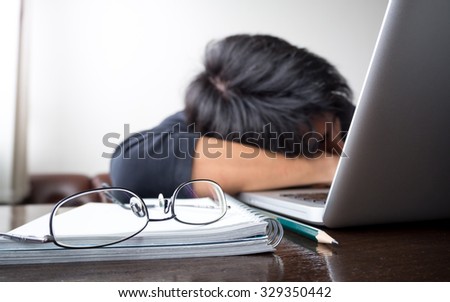 freelancer falling his face down taking a nap on wooden desk with laptop computer and notebook with eye glasses. concept of tired/lazy