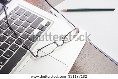 Eyeglasses on top of laptop keyboard with pencil and white paper on desk. business concept