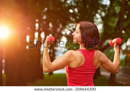 Aged woman working out with small dumbbells in the park in the morning.