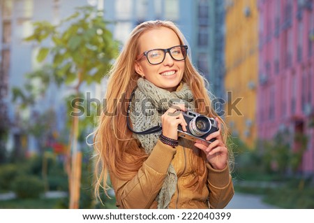 Outdoor closeup portrait of young pretty smiling blond woman holding old fashioned vintage camera
