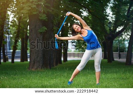 Happy middle aged caucasian brunette woman in blue sportswear stretching with blue jumping rope over her head outdoors smiling