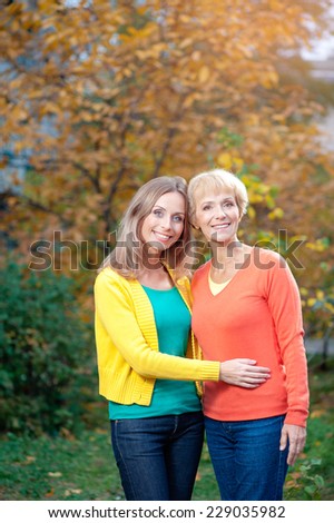 Portrait Of Middle aged Mother and her Adult Daughter smiling at camera in autumn park