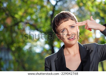 Close up portrait of stressful young caucasian business woman making gun with her hand pretending to blow up her head outdoors