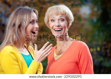 Portrait of adult Daughter talking to her surprised smiling mother wearing casual in the park