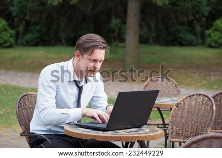 Excited businessman. Attractive young tired caucasian man in formal shirt and tie working on laptop while sitting at the table outdoors