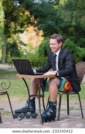Work and relax. Businessman dressed in suit, shorts and rollers working with laptop at the outdoors cafe
