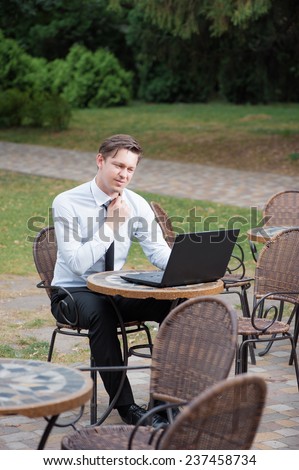 Hard working businessman. Attractive young tired man in formal shirt and tie working on laptop while sitting at the table outdoors
