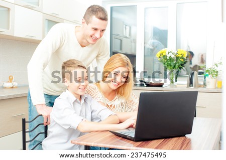 Happy caucasian family and digital technology. Boy and his smiling attractive mother and father using Laptop In Kitchen Together