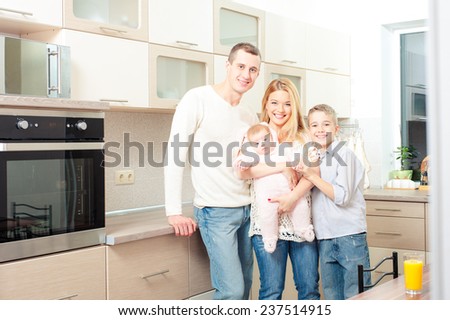 Happy caucasian family with teenage son and baby girl standing in kitchen together and smiling at viewer