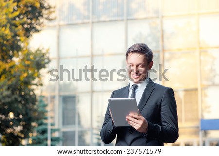 Businessman with digital tablet outdoors. Confident young man in formal wear working on digital tablet and smiling while standing against office building.