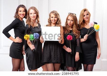 Your text here. Group of five smiling attractive woman in black dresses with white blank board banner indoors