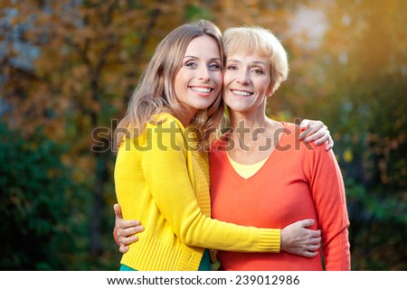 Outdoor portrait of  Pretty smiling Aged Mother and Adult Daughter Portrait Hugging in the autumn Park looking at camera