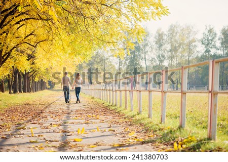 Romantic couple wearing jeans walking in autumn park, having a date at fall. Back view.