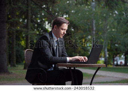 Focused businessman. Attractive young man in formal wear working on laptop while sitting at the table outdoors.