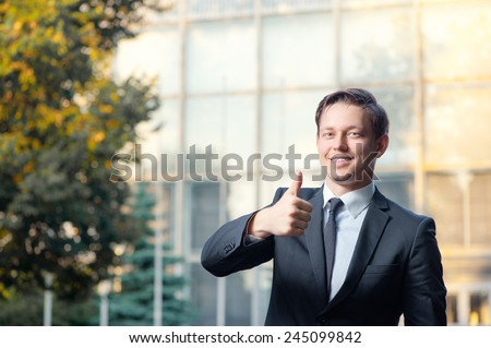 Great job! Happy young business man in formal wear showing his thumb up while standing against building structure