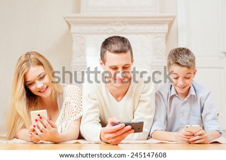 Happy family and digital technology. Attractive family couple and son lying on the floor using smart phones.
