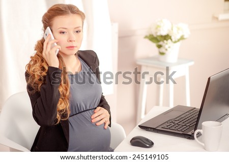 Pregnant business lady at work. Worried pregnant businesswoman talking on the phone while sitting at her working place in office