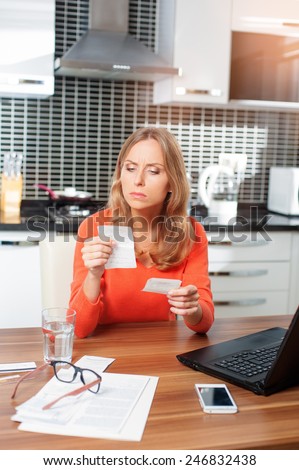 Nervous young caucasian woman looking at her financial debts in the kitchen at home