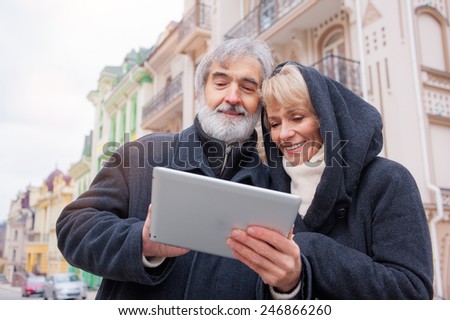 Attractive mature caucasian couple standing in urban street reading information on a tablet computer with a smile