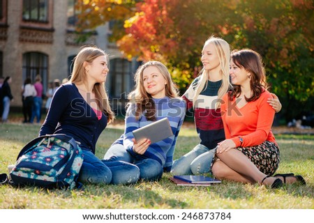 We love spending time together. Four happy caucasian young women spending time together while sitting in autumn park outdoors