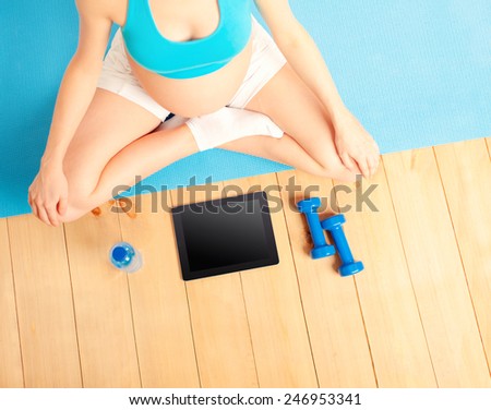 pregnant woman with dumbbells exercising with video course. Overhead of belly, dumbbells, digital tablet  and bottle of water.