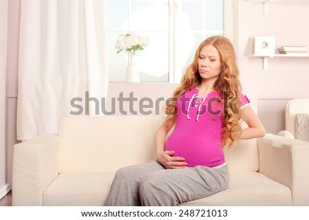 Attractive 7 months pregnant woman massaging her back sitting on the sofa