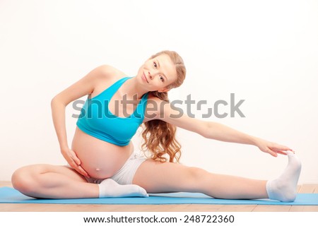 Prenatal exercises. Beautiful pregnant woman exercising stretching while sitting on mat