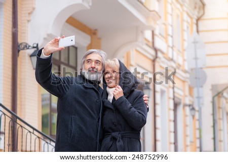 age, tourism, travel, technology and people concept - senior caucasian couple with camera phone taking selfie on street