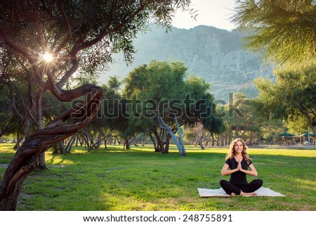 Morning yoga. Happy young woman in lotus pose in the park with mountains view.