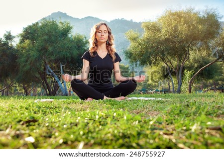 Morning meditation. Young woman with closed eyes in lotus pose in the park sitting on green grass