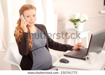 Pregnant business lady at work. Cheerful pregnant caucasian businesswoman talking on the phone while sitting at her working place in office