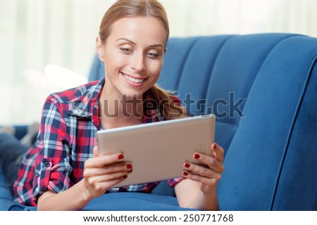 Young caucasian woman at home relaxing in her living room reading a digital tablet PC surf internet and work