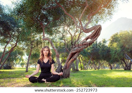 Morning meditation. Young woman in lotus pose in the park sitting on green grass.