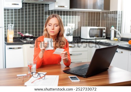 Nervous caucasian young woman looking at her financial debts in the kitchen at home